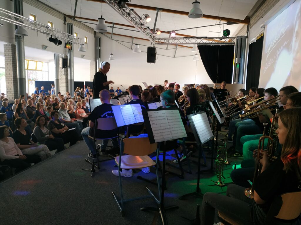 Musikveranstaltung mit Orchester und Publikum in einem Schulgebäude.