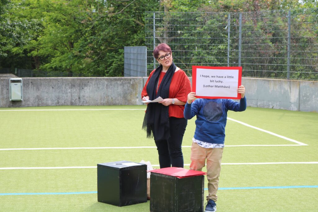 Frau mit Brille und Schal steht neben einem Kind, das ein Schild hält.