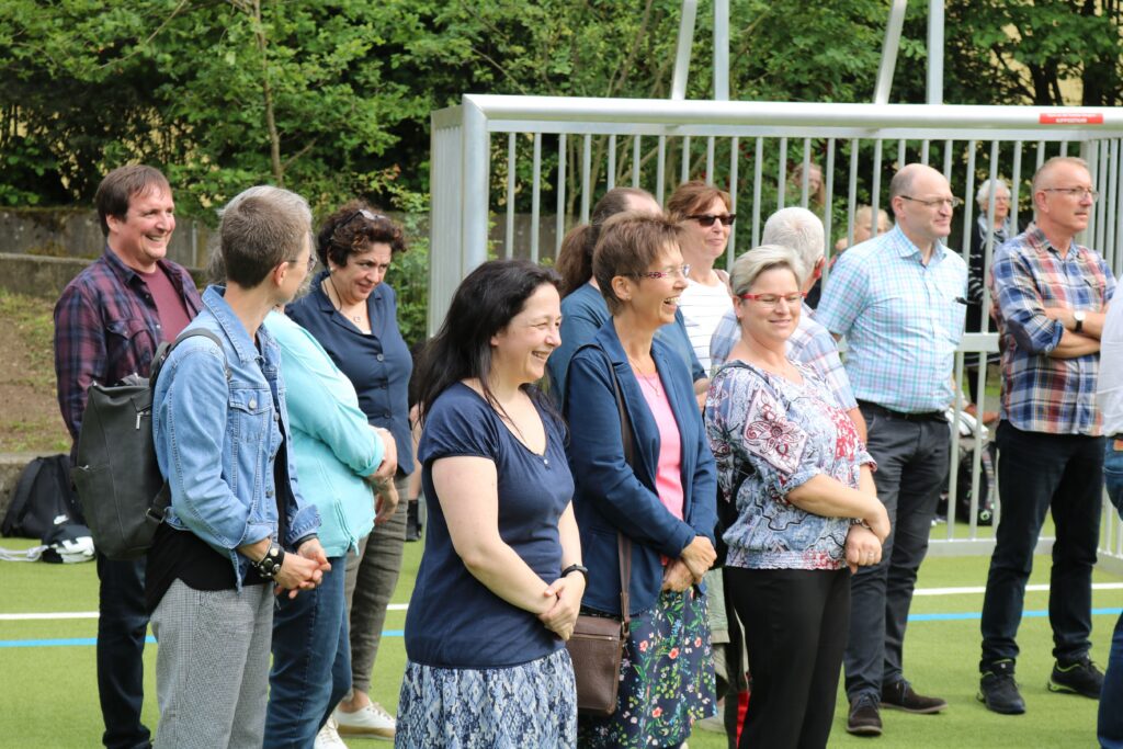 Gruppierung von Personen auf einem Sportplatz, alle lächeln und schauen nach vorne.