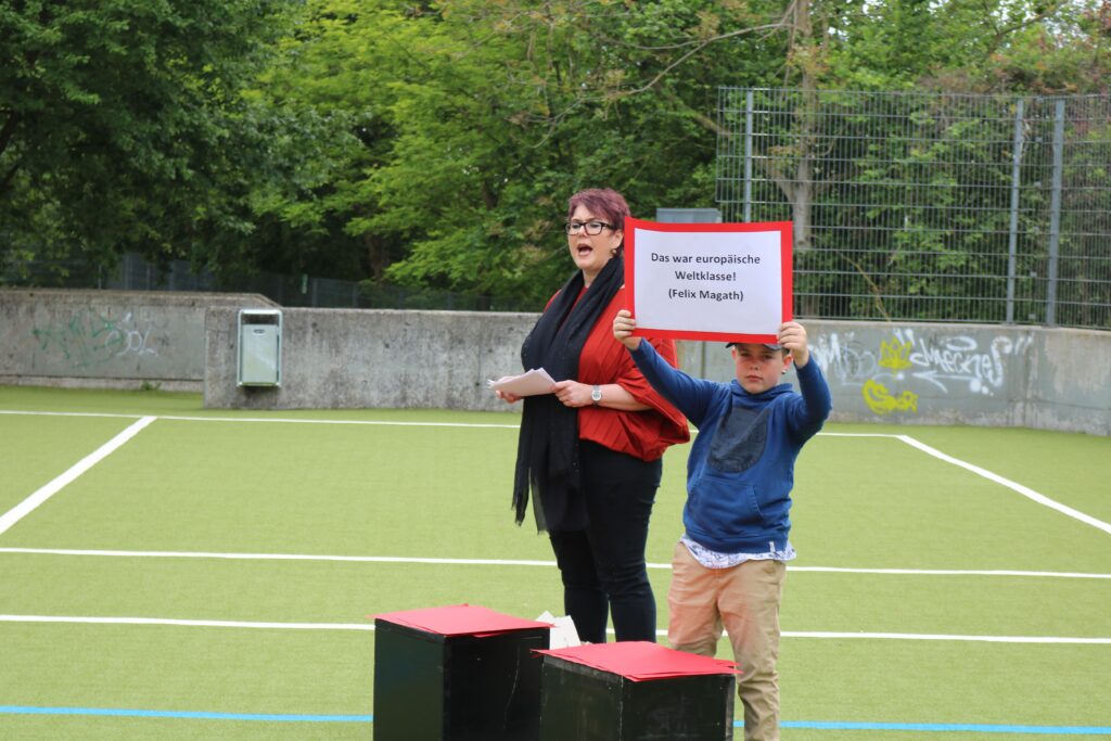 Person steht auf einem Sportplatz und hält ein Schild.