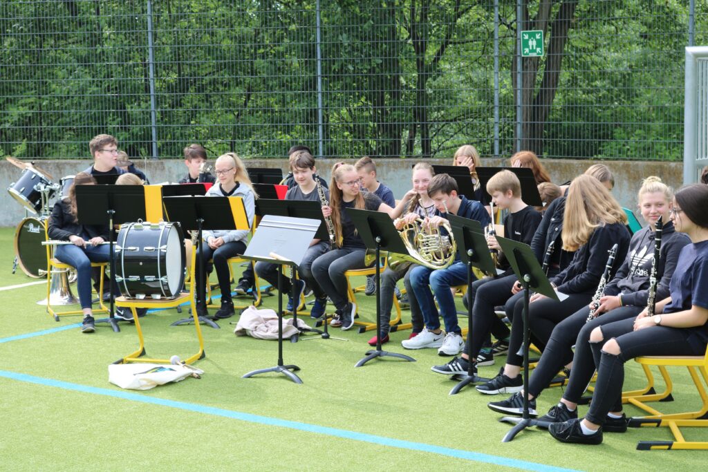 Schülerinnen und Schüler spielen in einer Musikklasse auf einem Sportplatz.