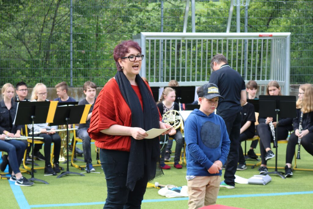 Eine Frau spricht zu einem Jungen, während im Hintergrund ein Blasorchester spielt.