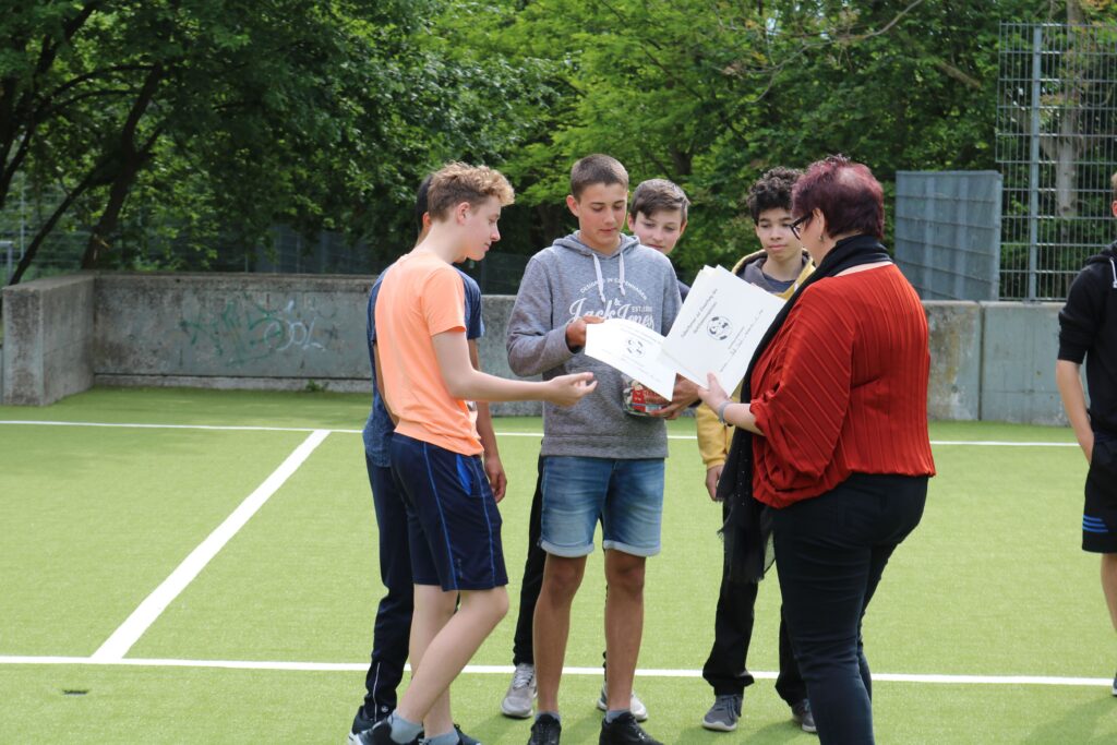 Schülerinnen und Schüler besprechen ein Projekt auf einem Sportplatz.