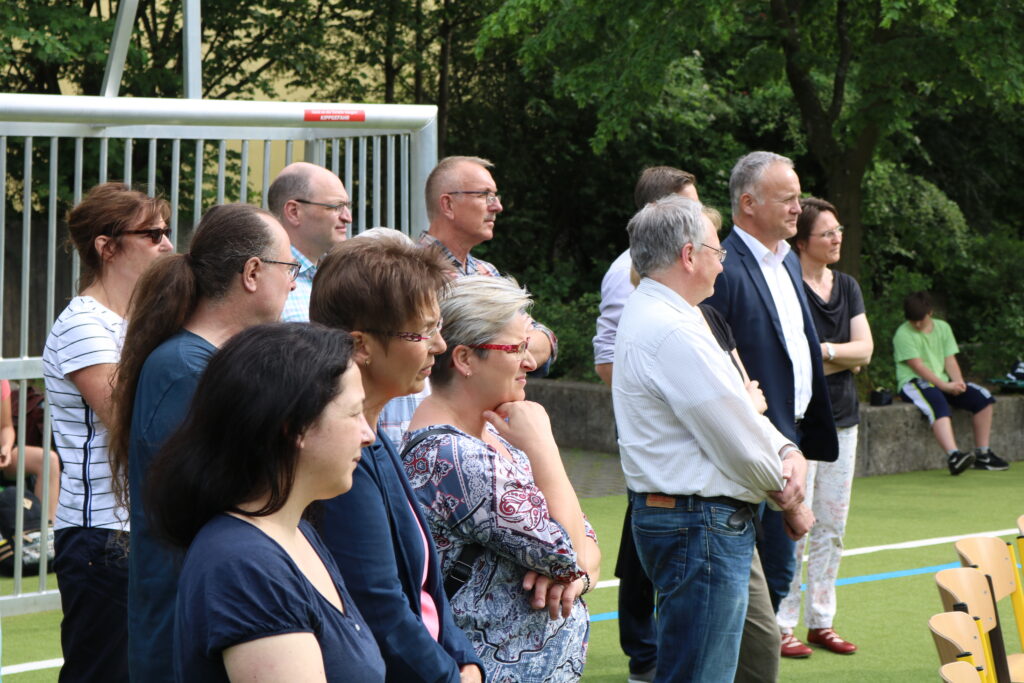 Gruppe von Personen steht aufmerksam auf einem Platz im Freien.