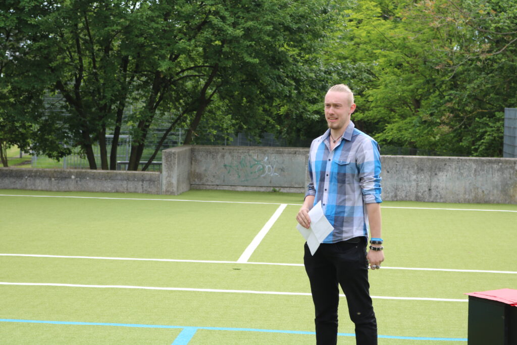 Ein Mann steht auf einem Sportplatz mit grüner Rasenfläche.