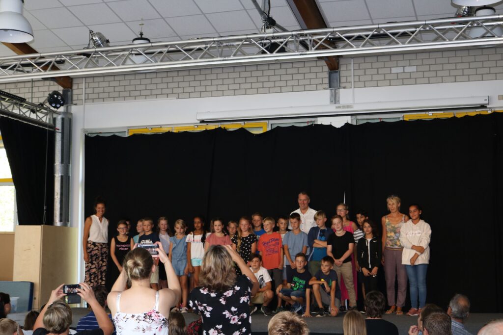 Schülerinnen und Schüler stehen auf der Bühne, während Gäste sie fotografieren.