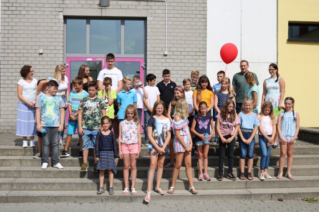 Schüler und Lehrer posieren auf Treppen vor der Schule, mit einem roten Ballon.