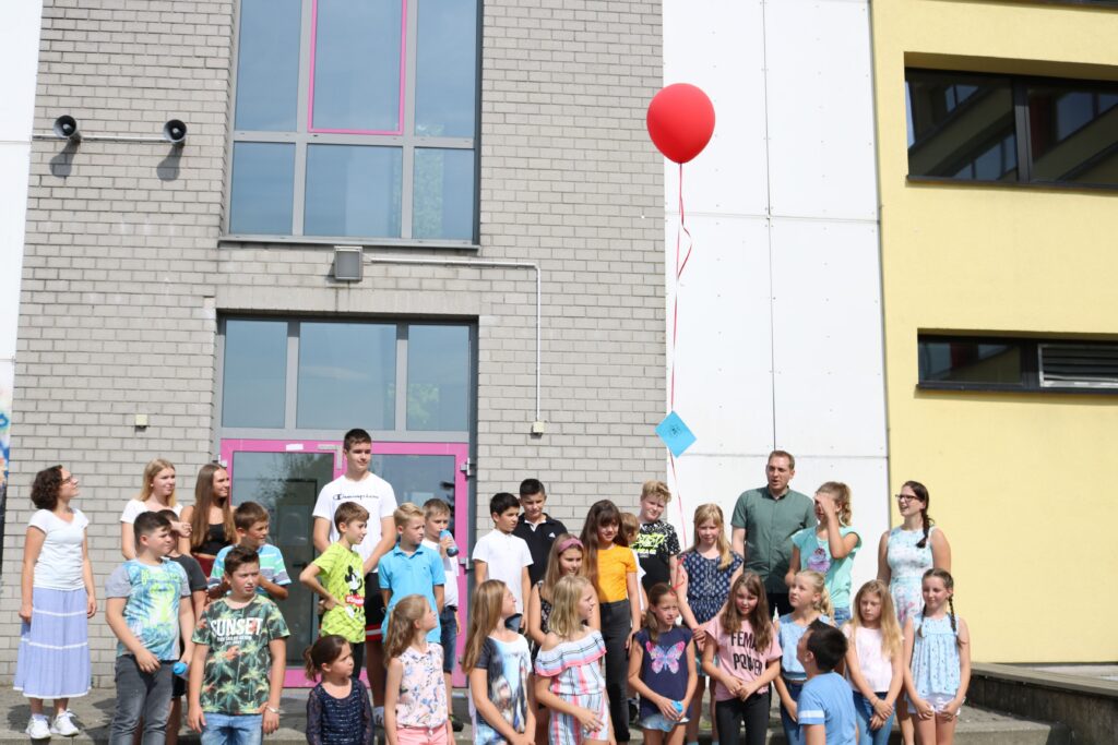 Gruppenfoto von Schülern und Lehrern vor einem Schulgebäude mit rotem Ballon.