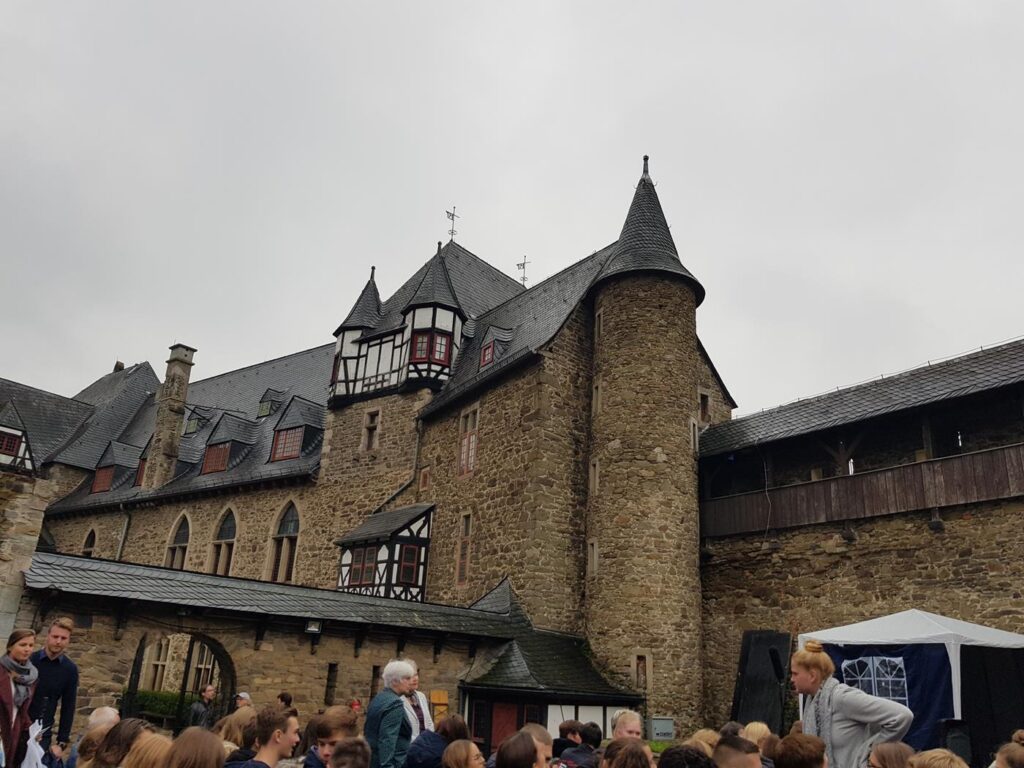 Historisches Schlossgebäude mit steilen Dächern und vielen Besuchern im Vordergrund.