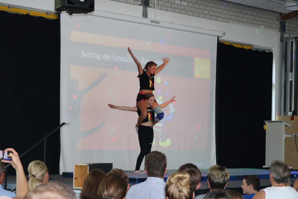 Zwei Tänzerinnen vor einer Präsentation auf einer Bühne in einer Schule.