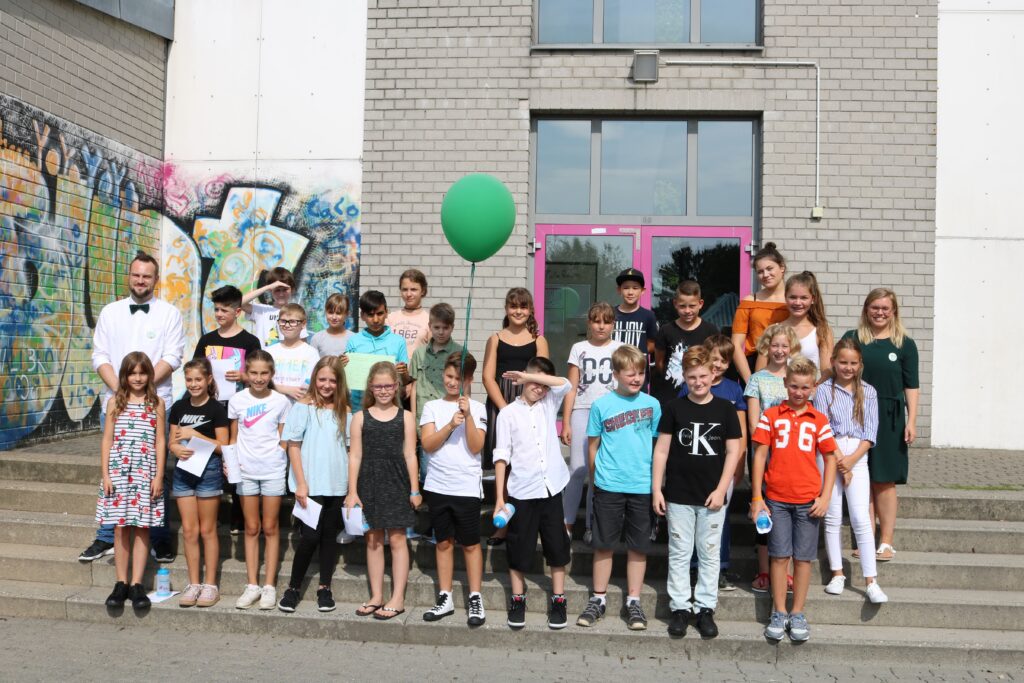 Gruppe von Schülern und Lehrern vor einem Gebäude mit Graffiti und Luftballon.