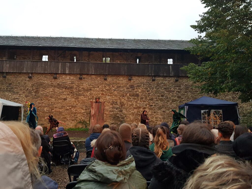 Theateraufführung vor einer alten Burgmauer mit Publikum.