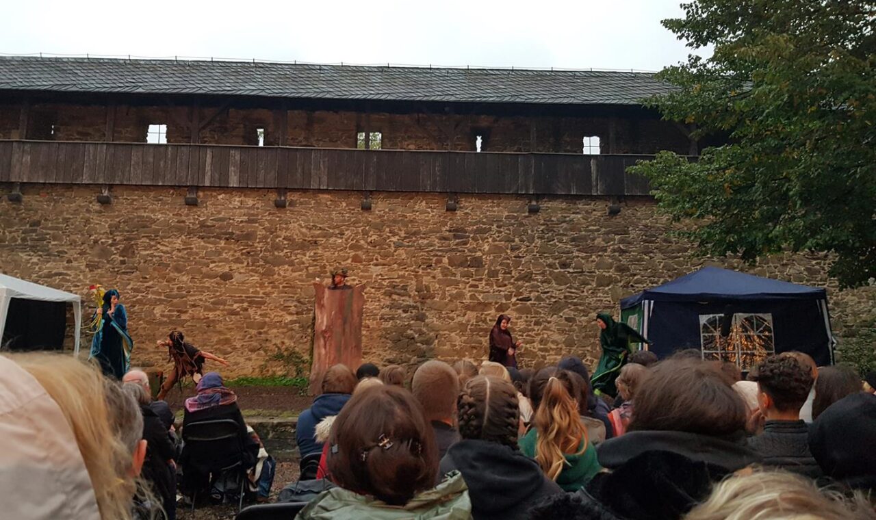 Theateraufführung vor einer alten Burgmauer mit Publikum.