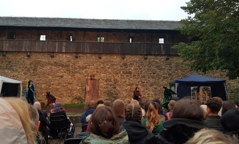 Theateraufführung vor einer alten Burgmauer mit Publikum.