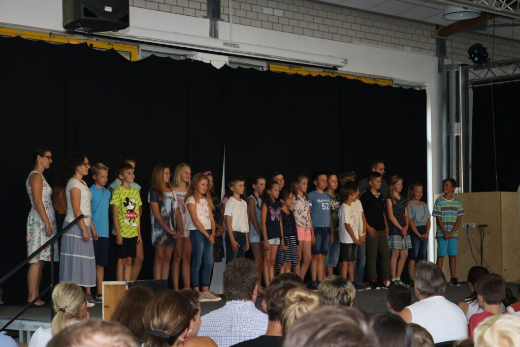 Schüler singen auf einer Bühne vor Publikum in einer Schwarzkulisse.