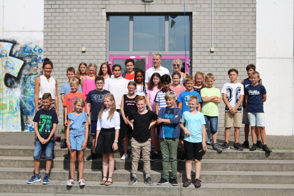 Gruppe von Schülern und Lehrern steht vor einem Gebäude.