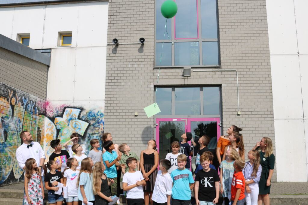 Schüler stehen vor einem Gebäude und schauen nach oben auf einen Luftballon.