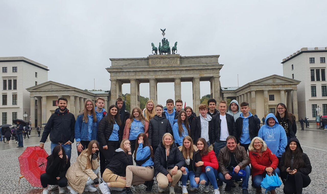 Gruppe von 25 Personen vor dem Brandenburger Tor an einem regnerischen Tag.