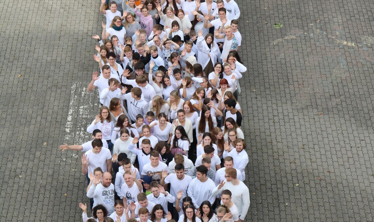 Schüler stehen in einer langen Reihe auf einem gepflasterten Platz.