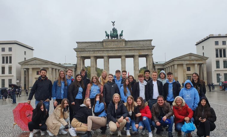 Gruppe von 25 Personen vor dem Brandenburger Tor an einem regnerischen Tag.