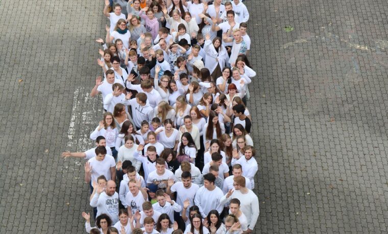 Schüler stehen in einer langen Reihe auf einem gepflasterten Platz.