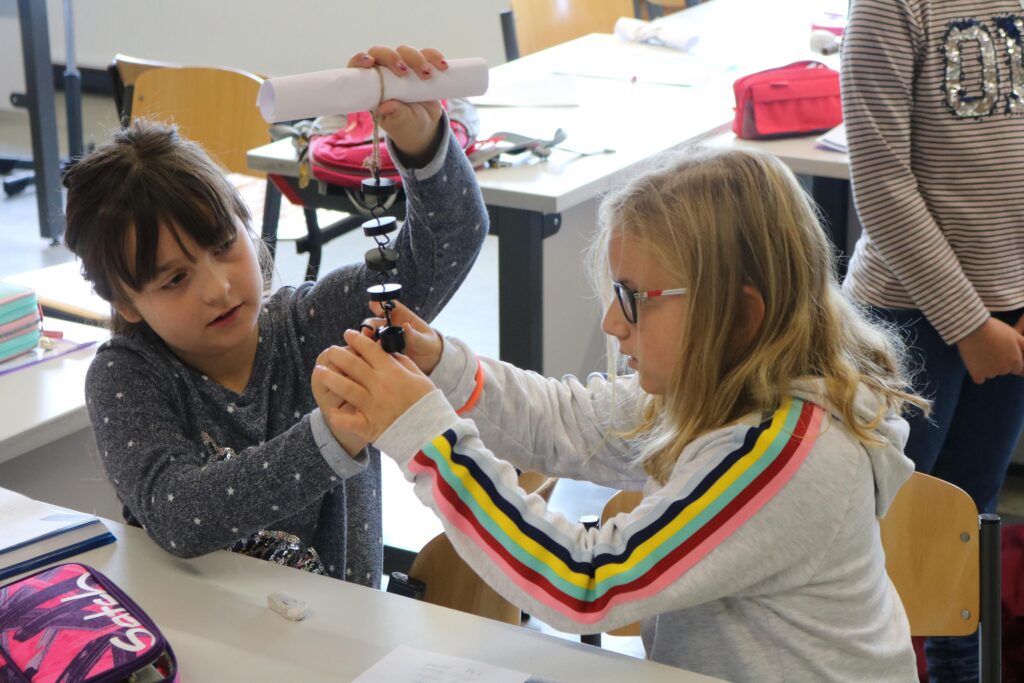 Zwei Schülerinnen experimentieren gemeinsam mit einem Experimentiergerät am Tisch.