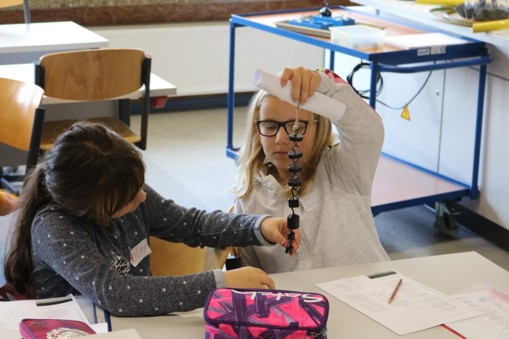 Schülerinnen führen ein Experiment mit einer Pendelaufhängung in einem Klassenzimmer durch.