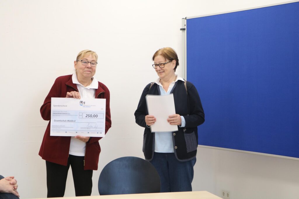 Zwei Frauen halten ein Zertifikat und eine Urkunde in einem Besprechungsraum.