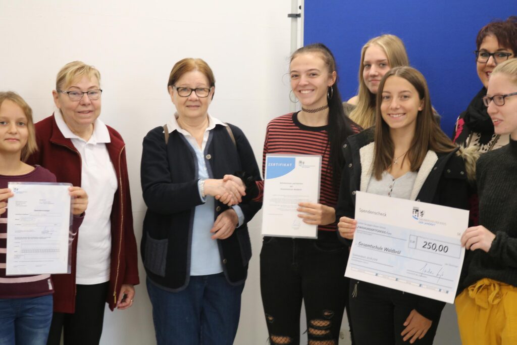 Übergabe von Urkunden und Schecks an Schüler in einem Raum.