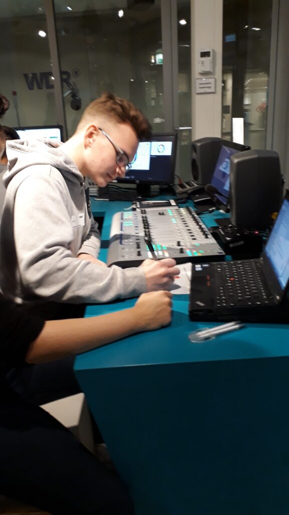 Ein Jugendlicher arbeitet konzentriert an einem Mischpult in einem Studio.