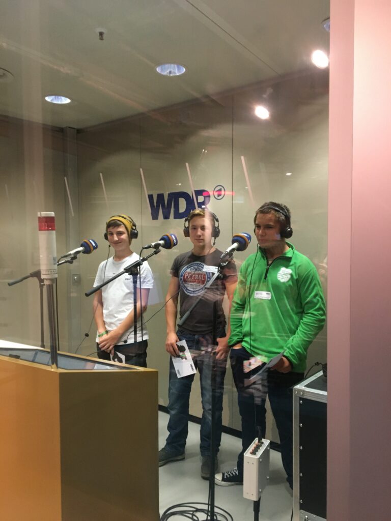 Drei Jugendliche stehen in einem Tonstudio vor Mikrofonen.