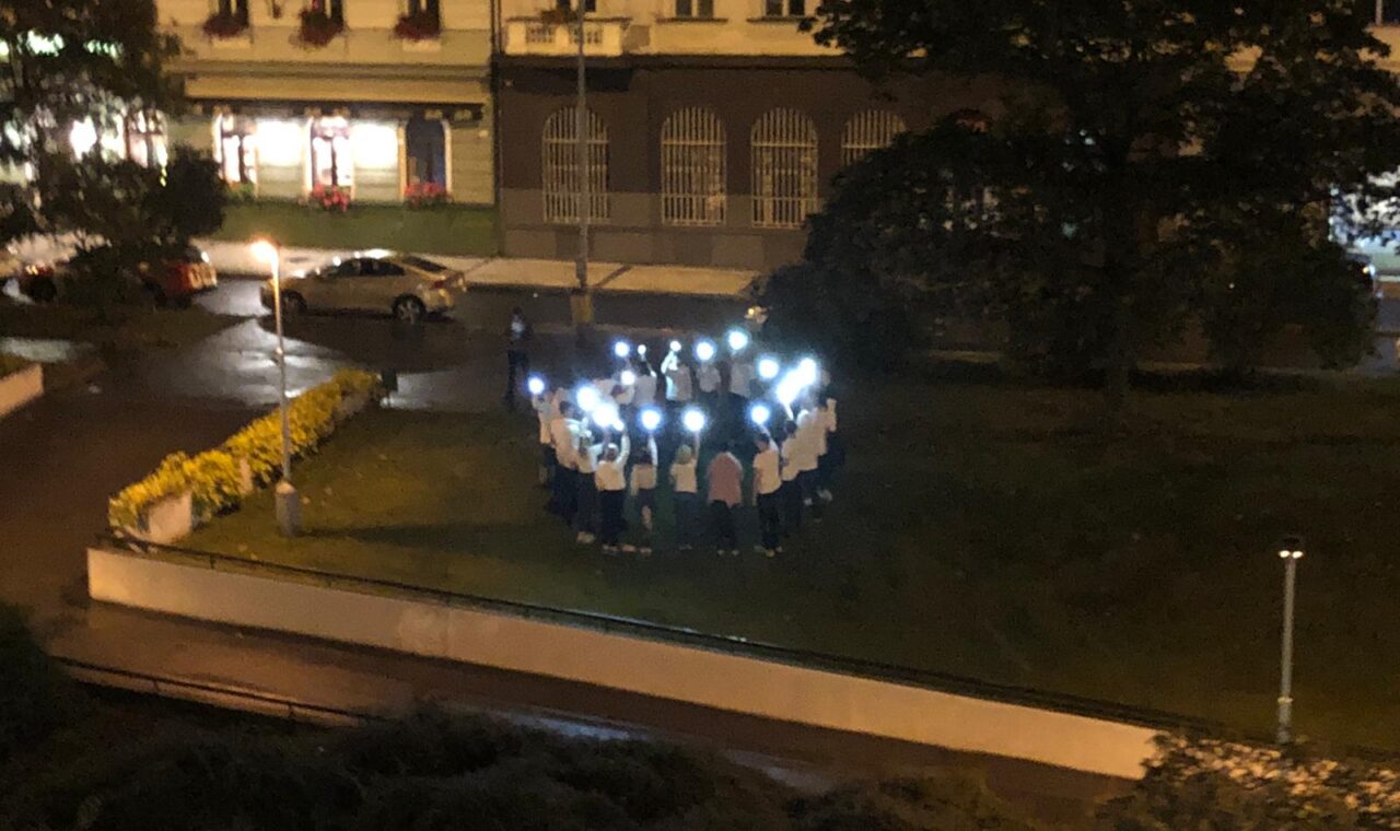 Gruppe von Menschen mit Handys in der Dunkelheit auf einer Wiese.