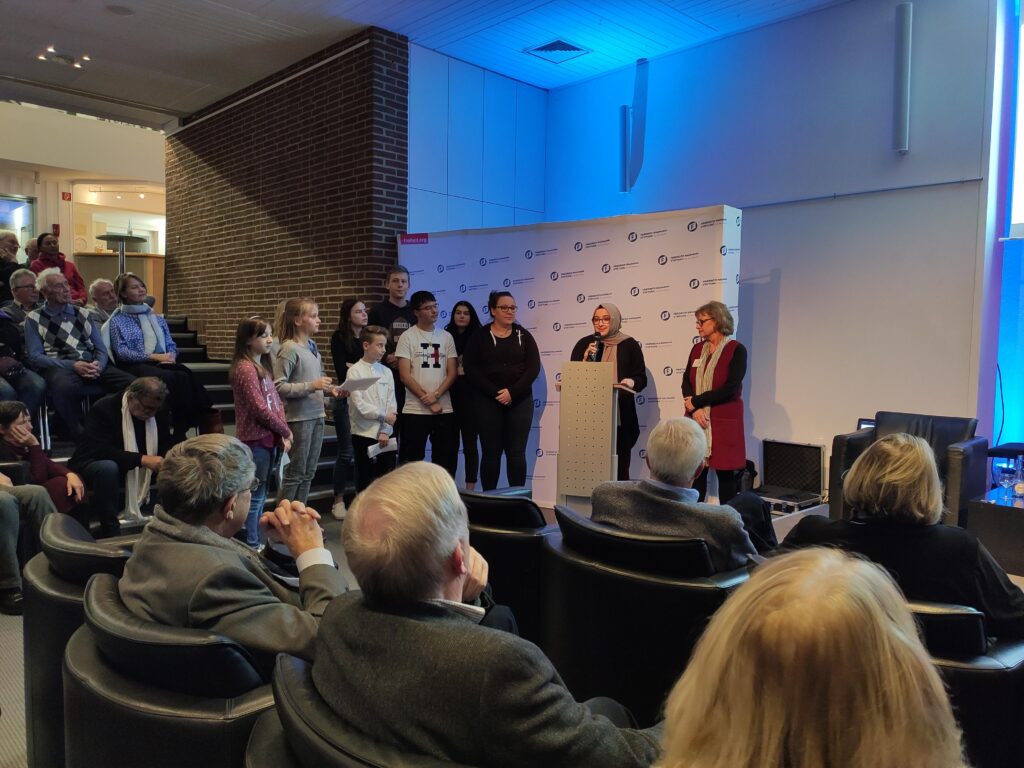 Gruppengespräch auf einer Bühne mit Publikum in einem Konferenzraum.