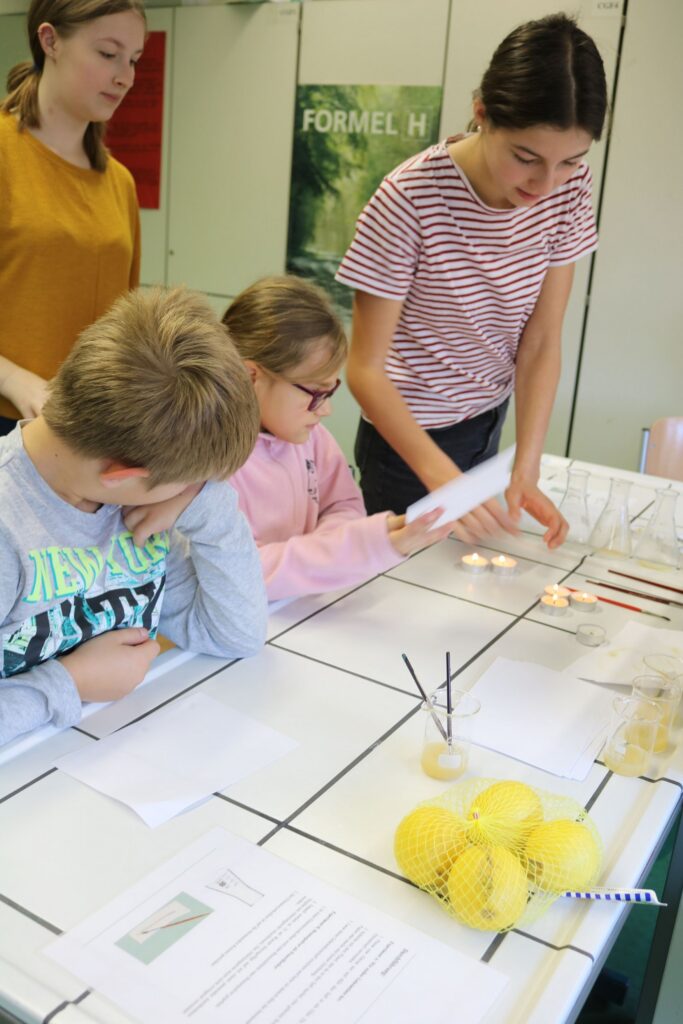 Schüler arbeiten an einem Experimentstisch, eine Lehrerin erklärt etwas.