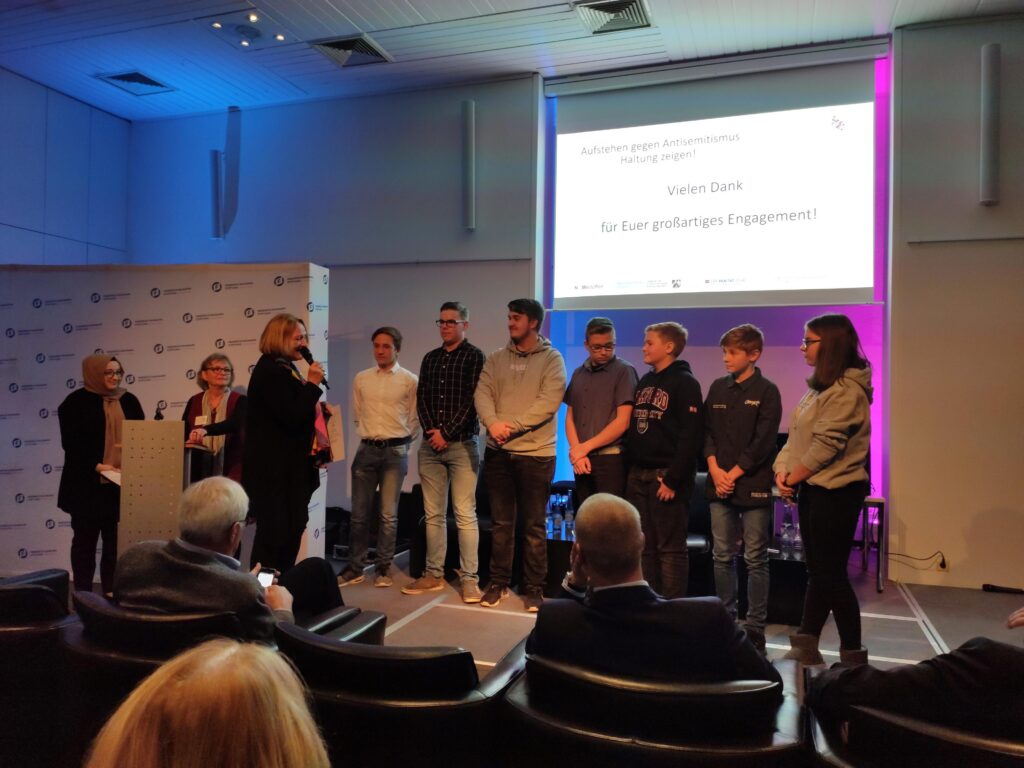 Gruppenvorstellung von Schülern bei einer Präsentation auf einer Bühne.