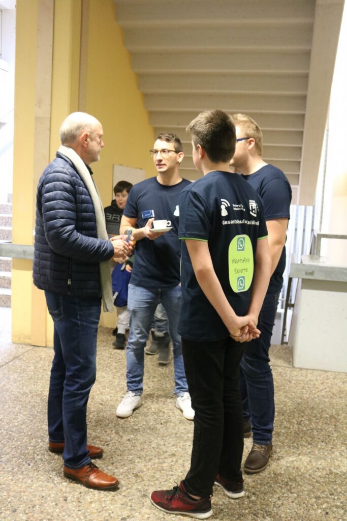 Personen in blauen T-Shirts im Gespräch in einem Flur.