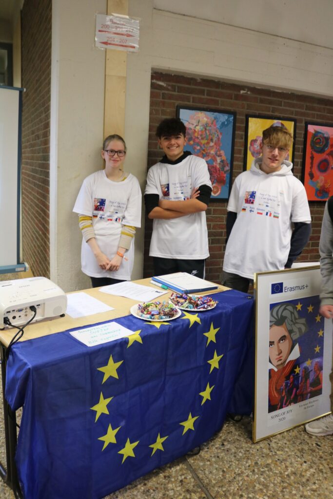 Schüler stehen an einem Tisch mit EU-Flagge und Informationsmaterialien.