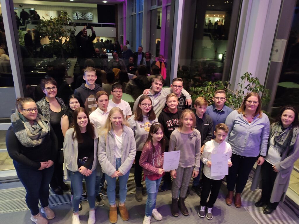 Gruppe von Schülern und Lehrern bei einer Veranstaltung in einem großen Raum.