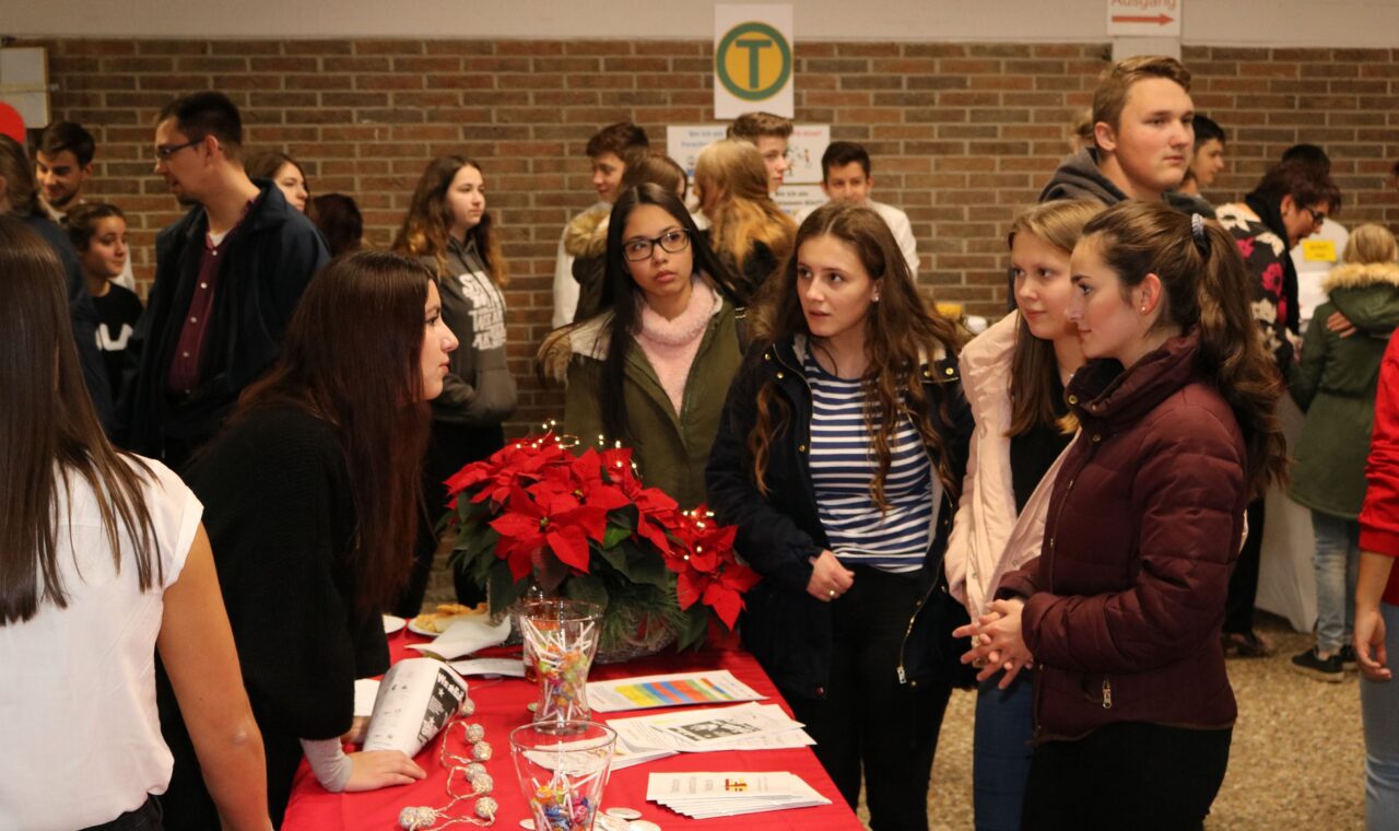 Schülerinnen und Schüler informieren sich an einem Stand. Weihnachtsdeko im Vordergrund.