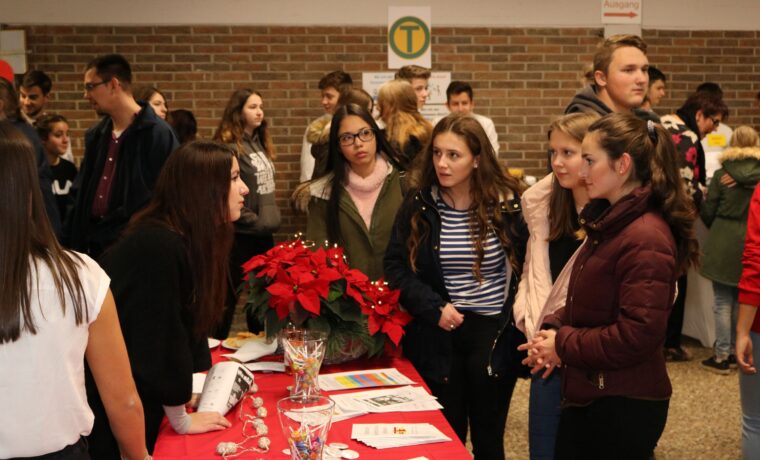Schülerinnen und Schüler informieren sich an einem Stand. Weihnachtsdeko im Vordergrund.