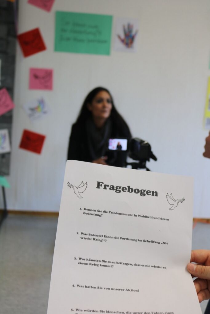 Schüler beantwortet Fragen vor einer Kamera; Fragenbogen im Vordergrund.