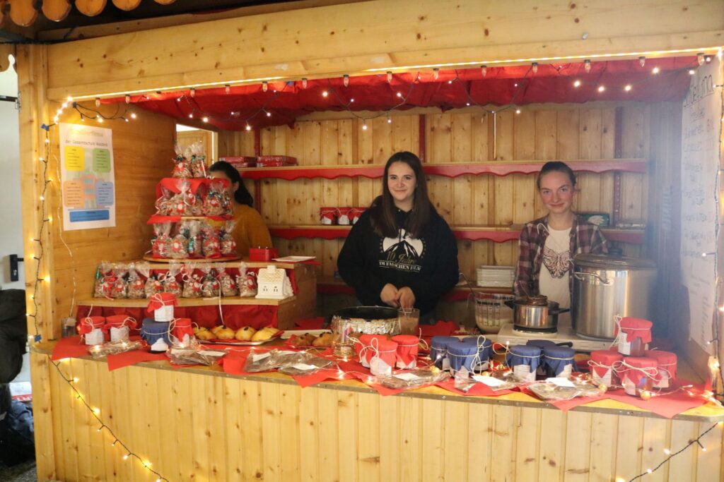 Weihnachtsmarktstand mit drei Verkäuferinnen und festlicher Dekoration.
