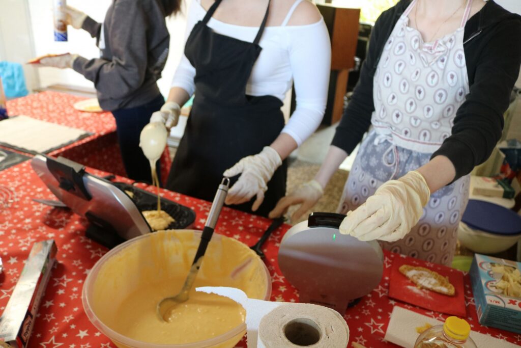 Schülerinnen backen zusammen und füllen Teig in Waffeleisen.