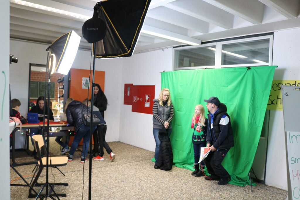 Gruppen von Schülern in einem Raum mit grünem Hintergrund für Fotoaufnahmen.