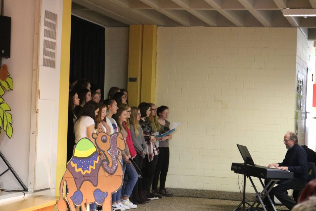 Schüler singen vor einem Klavier, im Hintergrund eine bunte Dekoration.