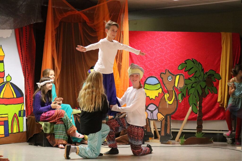 Schüler führen ein Theaterstück auf einer Bühne mit Kulissen vor.