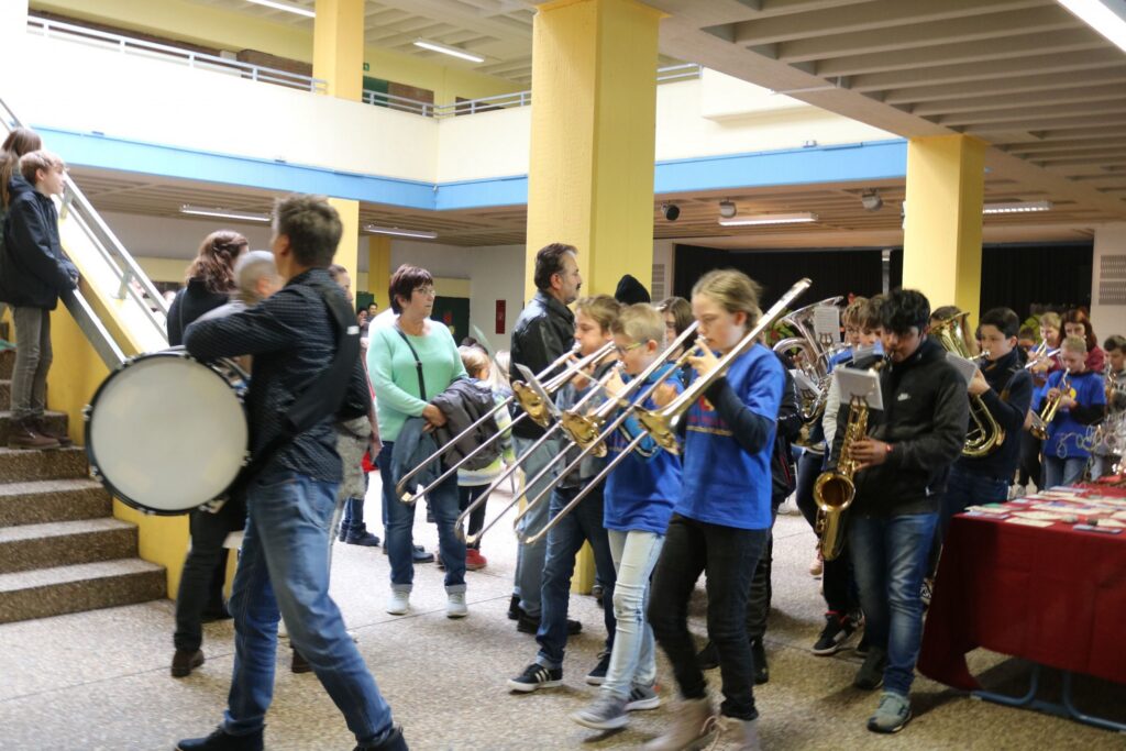 Schüler marschieren mit Instrumenten durch die Schule. Lehrer und Eltern schauen zu.
