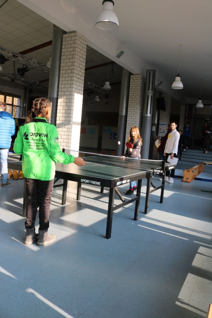Zwei Personen spielen Tischtennis in einer hellen Sporthalle.