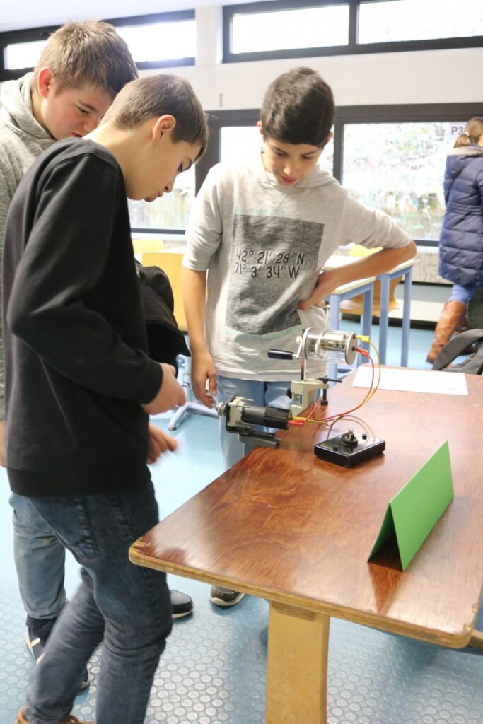 Drei Schüler arbeiten gemeinsam an einem technischen Gerät an einem Tisch.