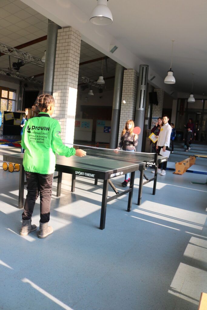 Tischtennistraining in der Turnhalle mit mehreren Schülern und einem Trainer.